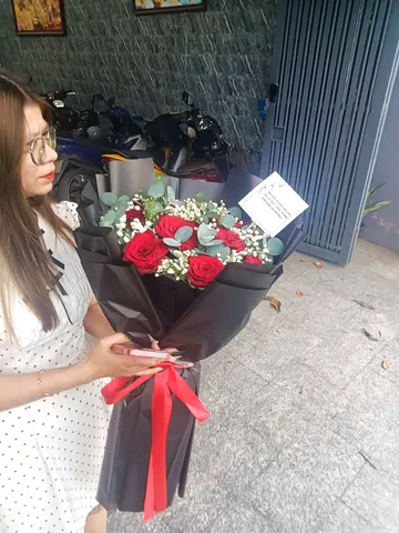 Khách nữ nhận bó hoa hồng đỏ bọc giấy đen thắt nơ đỏ