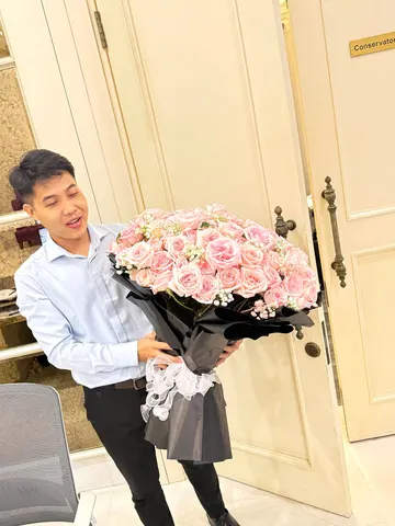 Khách nam nhận bó hoa hồng phấn bọc giấy đen do Hoarosa giao tận nơi
