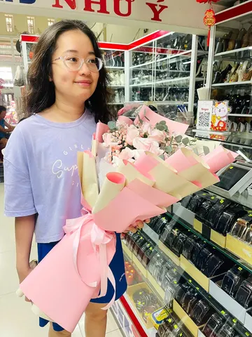 Khách nữ nhận bó hoa hồng phấn bọc giấy hồng kem