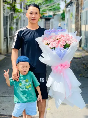 Khách nam cùng bé nhận bó hoa hồng phấn bọc giấy trắng mừng sinh nhật