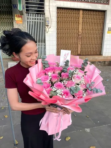 Khách nữ cười tươi nhận bó hoa hồng tone hồng bọc giấy hồng