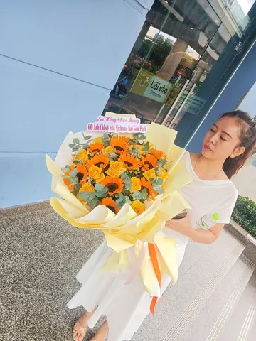 Khách nữ nhận lẵng hoa tone cam vàng chúc mừng